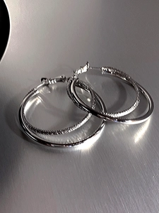 Detailed macro view of silver double-layered hoop earrings with woven texture finish