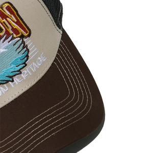 Gros plan sur la broderie aigle d'une casquette trucker beige avec visière brune