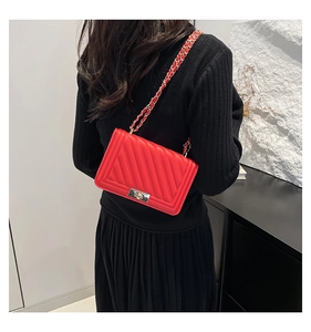 Detail of red quilted shoulder bag with gold chain strap and metal lock on a model