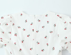 Detail von Karree-Ausschnitt und Puffärmeln am weißen Kleid mit rotem Rosenmuster