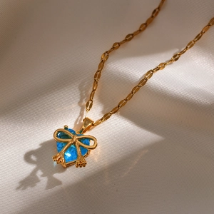 Close-up of gold bow necklace with a blue heart-shaped crystal on white fabric
