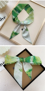 Macro view of silky green abstract painted scarf styled in a gift box and golden tray
