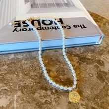 Dettaglio collana di perle con ciondolo dorato su un libro blu e marmo marrone scuro