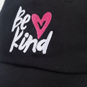 Macro detail of Be Kind embroidery and pink heart on black cotton baseball cap