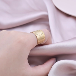 Detailed view of wide gold ring with sunburst texture worn on a satin background