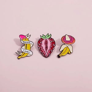Three creative fruit enamel pins including banana and strawberry designs on pink background