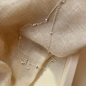 Close-up of a S925 sterling silver necklace with heart charms on beige fabric