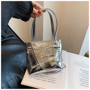 Detail of silver metallic handbag featuring decorative bows and metal chain strap