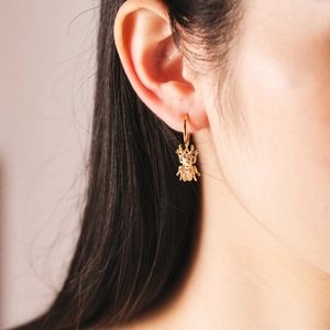 Créole minimaliste dorée en forme d'insecte avec pierres roses sur modèle féminin