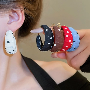 Close-up of C-shaped polka dot fabric wrapped hoop earrings on a model in white