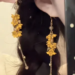 Long tassel earrings with yellow flowers and fine gold chains worn by a model