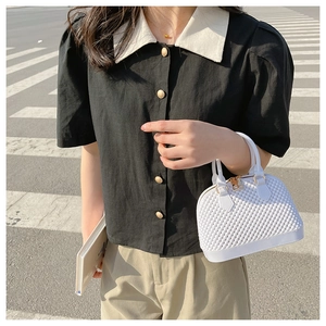 Close-up of a white quilted crossbody shell bag held by a model on a street background
