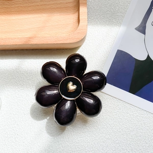 Close-up of black 3D flower phone grip with a golden heart center on a wooden tray