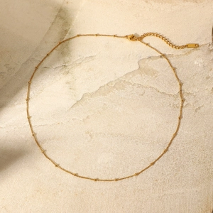 Dettaglio di una collana a catena a sfere dorate con chiusura a moschettone su pietra beige