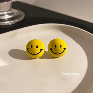 Minimalist yellow smiley face stud earrings on a white ceramic tray with warm lighting