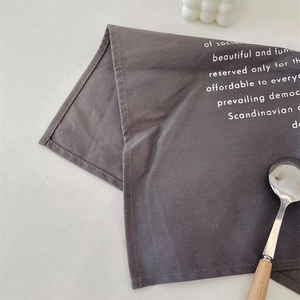 Close-up of a dark grey linen table mat with white text and rustic wooden spoon detail