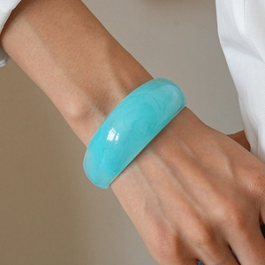 Detail of wide sky blue resin bangle with marble texture worn on model wrist