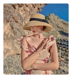 Outdoor shot of raffia sun hat with black ribbon detail on a scenic rocky beach