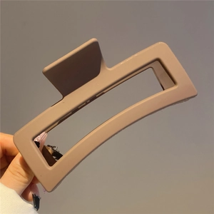 Detailed view of large brown matte resin hair claw clip held by hand against grey wall