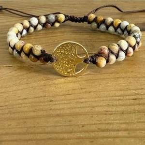 Detail eines gewebten Perlenarmbands mit goldenem Lebensbaum auf rustikalem Holz