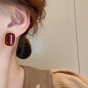 Detail of a vintage burgundy square stud earring with gold plating on a model