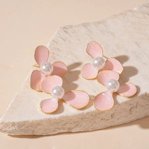 Close-up of pink flower earrings with pearls and gold edges on stone background