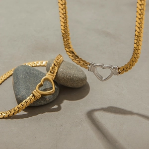 Detail of luxury gold curb chain necklace and bracelet with heart pendants on natural stone
