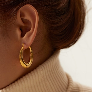Close-up of chunky gold hoop earrings in polished stainless steel worn by a model