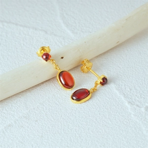 Close-up of 925 sterling silver earrings with oval red gemstones and golden chain details