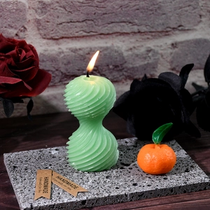 Dettaglio della candela a spirale verde accesa e mini candela arancione su pietra
