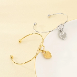 Detail view of gold and silver knot bangles with heart charms on minimalist background