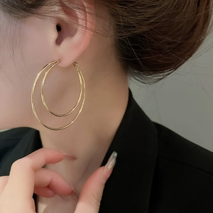 Detail of double-layered golden round hoop earrings worn by a model with a dark suit