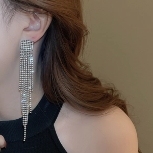 Close-up of sparkling rhinestone long tassel earrings worn by a model in warm lighting