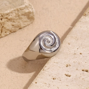 Macro detail of polished stainless steel ring showing spiral texture on beige stone