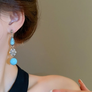 Close-up of elegant turquoise teardrop earrings with silver flower detail on model