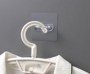 Self-adhesive wall hook holding a white hanger and shirt on a textured gray background