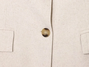 Dettaglio macro del blazer in lino beige con bottone tartarugato e finitura tasca