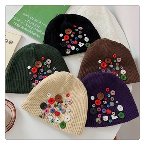 Flat lay of colorful button-decorated knitted beanies in black, green, brown, and beige