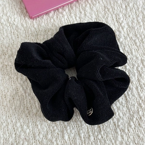 Detail of a soft black towel cloth scrunchie with a round handmade metal tag on white fabric