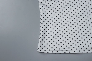 Detail view of white knitted fabric with black polka dots and high-quality edge stitching