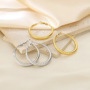 Macro shot of gold and silver hoop earrings with spiral texture on marble and silk