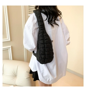 Détail d'un sac bandoulière noir matelassé porté par un mannequin en chemise blanche