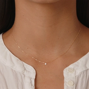 Close-up of a delicate gold S925 sterling silver necklace with a single zircon on a model