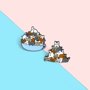 Detail of stacked cartoon cat enamel pins and cat cup brooch on pastel background