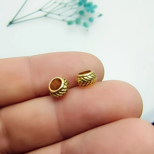 Macro detail of gold alloy spacer beads with textured grain pattern on a fingertip