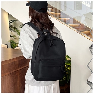 Rear view of a minimalist black backpack worn by a model in a modern home setting