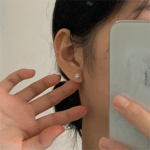 Close-up of minimalist silver flower earring with white enamel petals on model ear