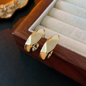 Close-up of irregular multi-layer golden C-shaped metal earrings on a dark wood box