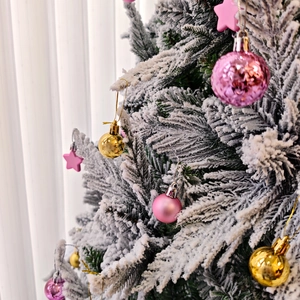 Gros plan d'ornements roses et dorés sur une branche de sapin de Noël enneigée