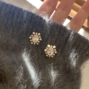 Detail shot of flower earrings with zircons and pearls on grey sweater texture